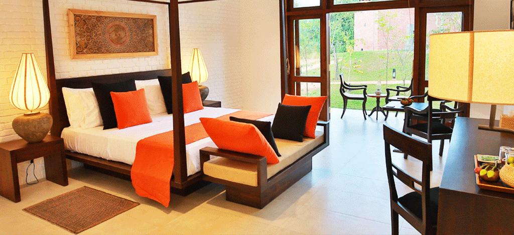 A white-walled room with a dark four-poster bed, orange cushions and glass doors to the garden.